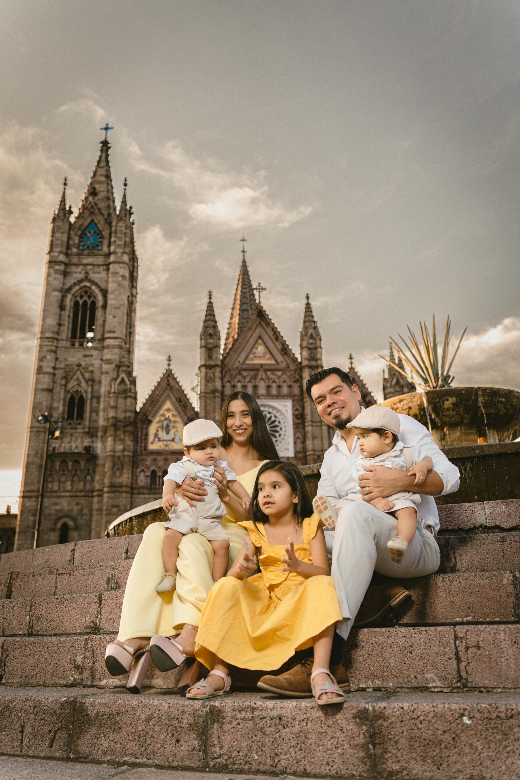 Family of five smiling and posing on steps in front of a historic gothic-style church.